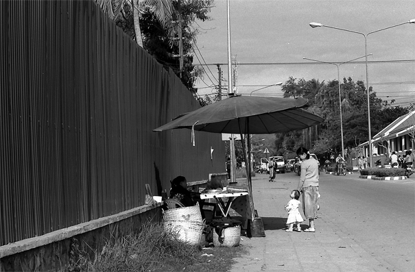 Mother And Her Baby In Front Of A Food Stall (Laos)
