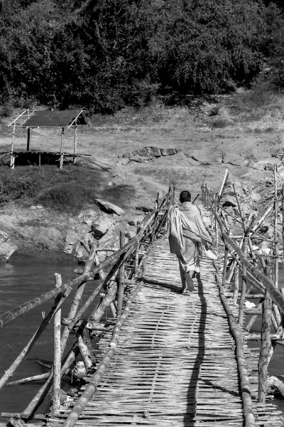 Buddhist monk crossing bamboo bridge