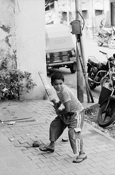 Boy Holding A Bat On The Sidewalk (India)
