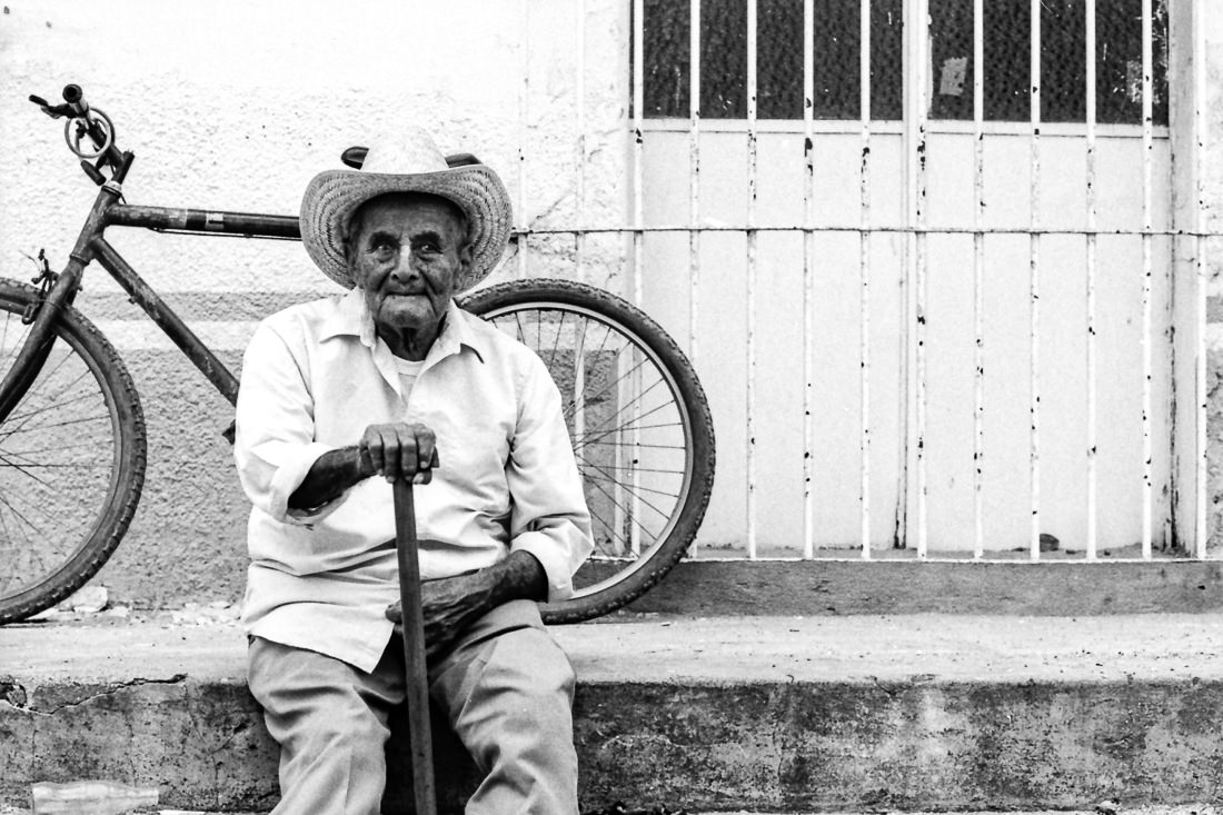 Old man with cowboy hat sitting by roadside