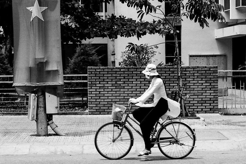 道路脇に掲げられたベトナム国旗の前を通り過ぎる自転車