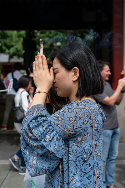 Woman pressing hands while gripping incense sticks