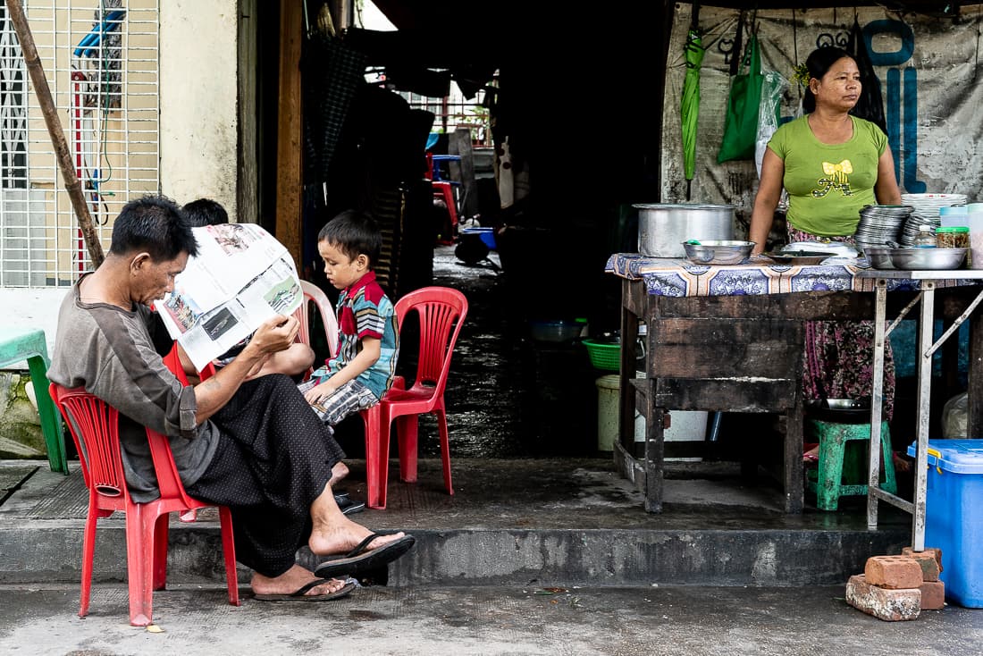 Man reading newspaper at a food stall in Yangon
