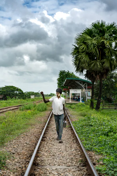 Young man walking on railway track with lunch box