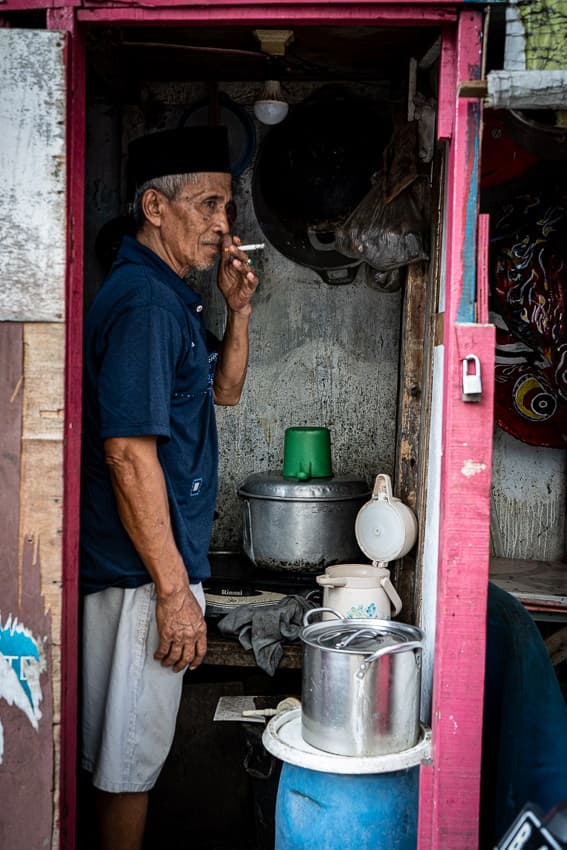 Man with a cap called Songkok smoking a cigarette in the hut