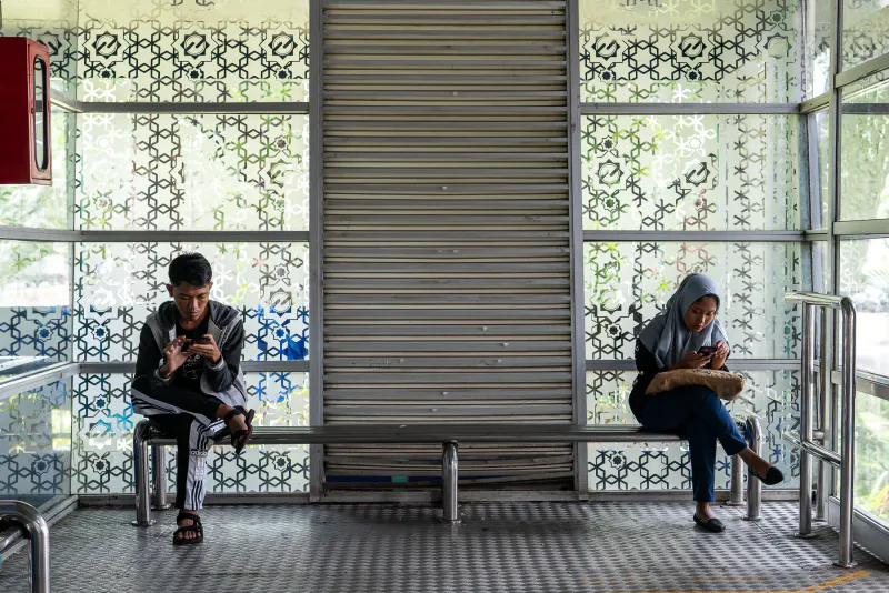 バス停のベンチでスマホをいじる男と女