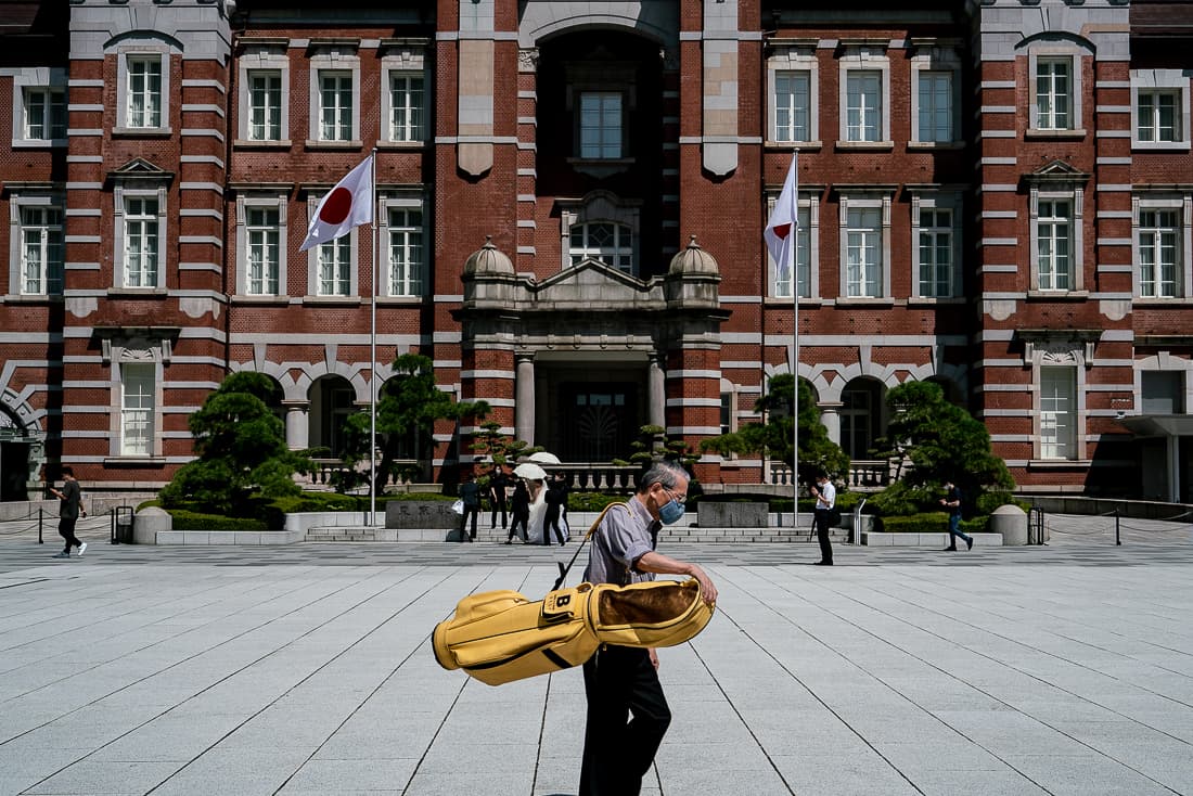 ゴルフバッグを抱えながら東京駅前を歩く男性