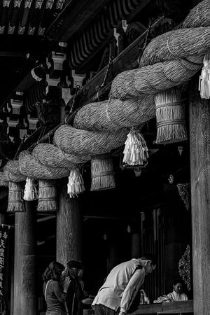 寒川神社の太い注連縄の下でお辞儀する男