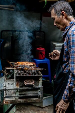 Man grilling fishes in Tha Tien Market