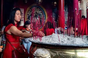 Woman in a red dress sticking red incense sticks in Jin De Yuan