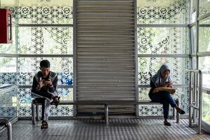 Man and woman fiddling with their phones on a bench at a bus stop