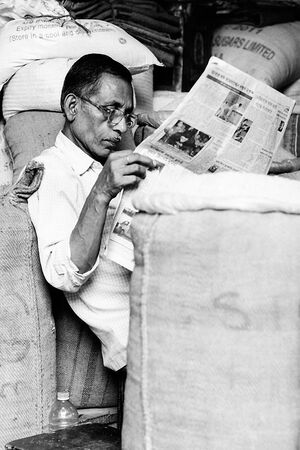麻袋に囲まれて新聞を読む男