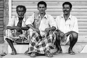 Three men sitting together in front of shutter