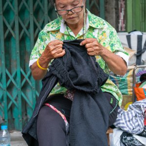 歩道で縫い物をする老婆