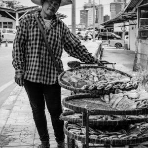 Woman selling dried fishes on sidewalk