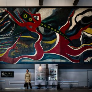 Man stopping under big wall painting by Taro Okamoto