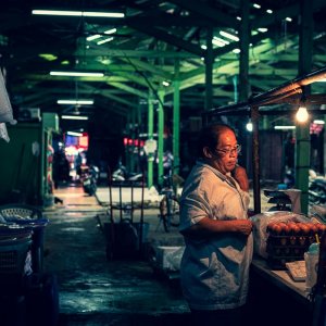 Man standing in a dim passage in Khlong Toei Market in Bangkok. The place seemed to be his shop. A bare bulb was lighted. And some row uncooked eggs were seen on the counter.