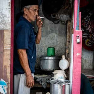 Man with a cap called Songkok smoking a cigarette in the hut