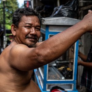 Shirtless man raising his arm up in front of a food stall
