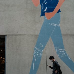 Man walking in front of a wall with a woman walking