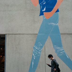 Man walking in front of a wall with a woman walking