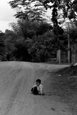 Boy sitting down on the edge of dirt road