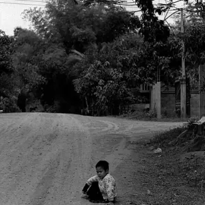 Boy sitting down on the edge of dirt road