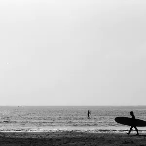 Silhouetted man carring surfborad