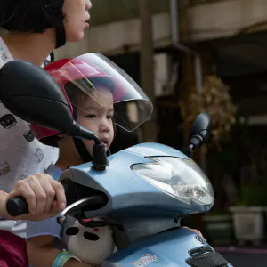 A boy riding a motorcycle with his mother