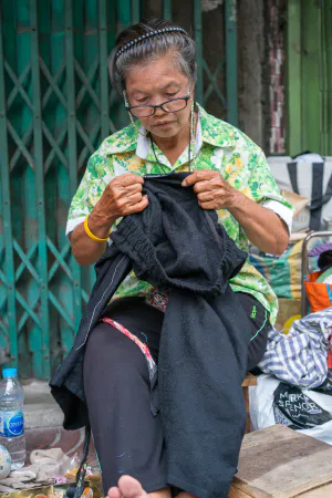 歩道で縫い物をする老婆