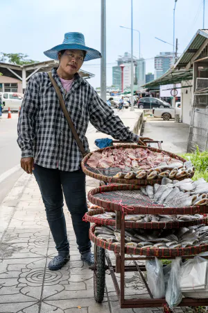 Woman selling dried fishes on sidewalk