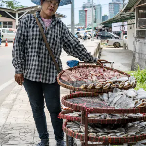Woman selling dried fishes on sidewalk