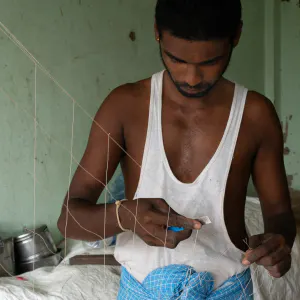 Man repairing fishnet with razor
