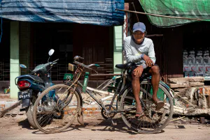 Young man waiting for customers with sitting on well-worn pedicab