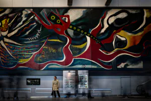 Man stopping under big wall painting by Taro Okamoto