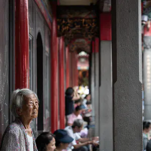 Older woman standing with beadrolls in her hands in Lungshan Temple