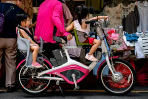 Two little girls riding on same bicycle in front of shop