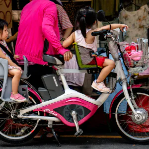 Two little girls riding on same bicycle in front of shop