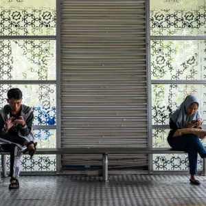 Man and woman fiddling with their phones on a bench at a bus stop