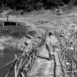 Buddhist monk crossing bamboo bridge