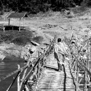 Buddhist monk crossing bamboo bridge