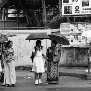 Women waiting at bus stop with putting umbrella up