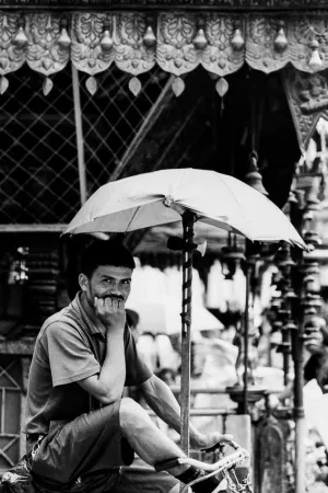 Rickshaw wallah waiting for customer under umbrella