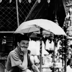 Rickshaw wallah waiting for customer under umbrella