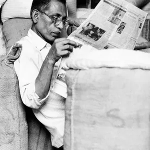 麻袋に囲まれて新聞を読む男